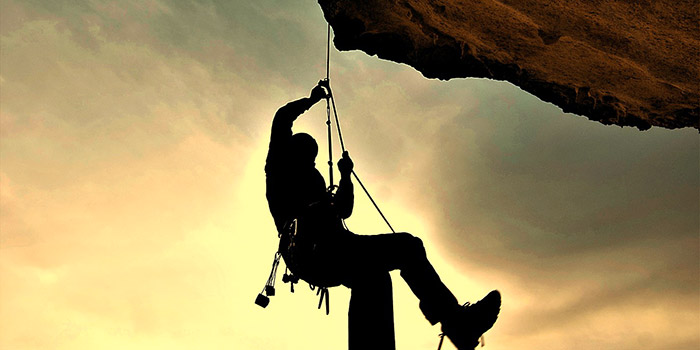 Image d'un grimpeur en plein effort, silhouetté contre un ciel doré au coucher du soleil, symbolisant l'esprit d'audace et de liberté en montagne.