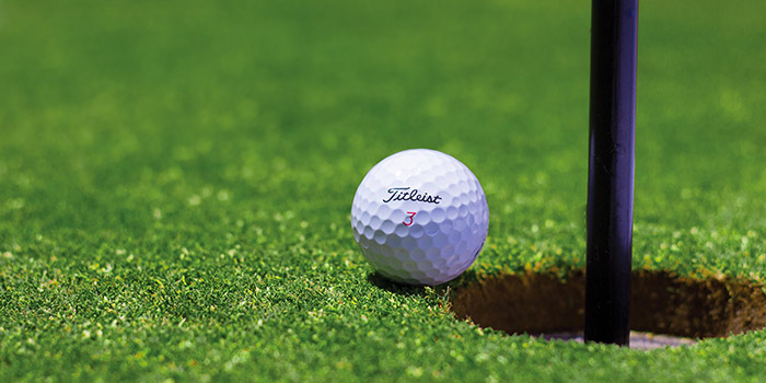 Image d'une balle de golf Titleist à côté du trou sur un green impeccable, illustrant l'intensité et la précision nécessaires pour un putt réussi.