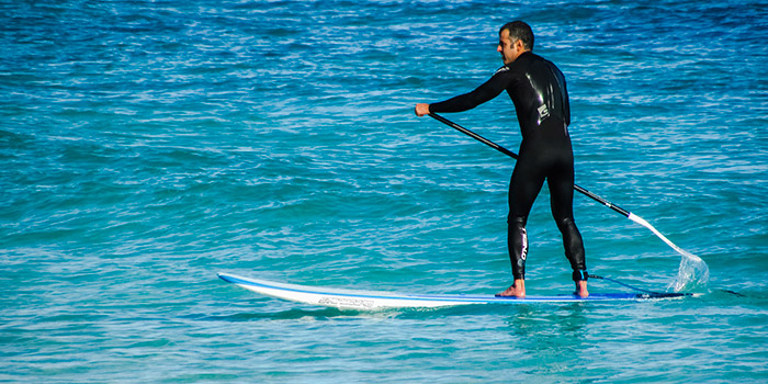 Homme faisant du paddle sur des eaux turquoise scintillantes, capturant la beauté des sports nautiques et l'harmonie avec la nature.