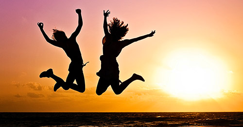 Freudensprung-am-Strand-bei-Sonnenuntergang Moment der Freiheit und überwältigenden Freude bei Sonnenuntergang am Strand, mit springenden Freunden, eingehüllt in leuchtende Farben.