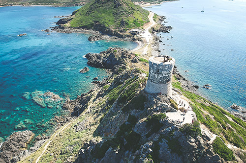 Phare majestueux sur promontoire rocheux surplombant une mer cristalline, sous un ciel serein.