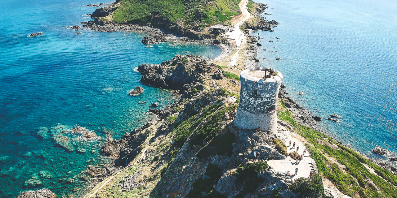Image d'une tour historique surplombant les eaux cristallines de la mer Méditerranée à Ajaccio, Corse, entourée de falaises rocheuses.