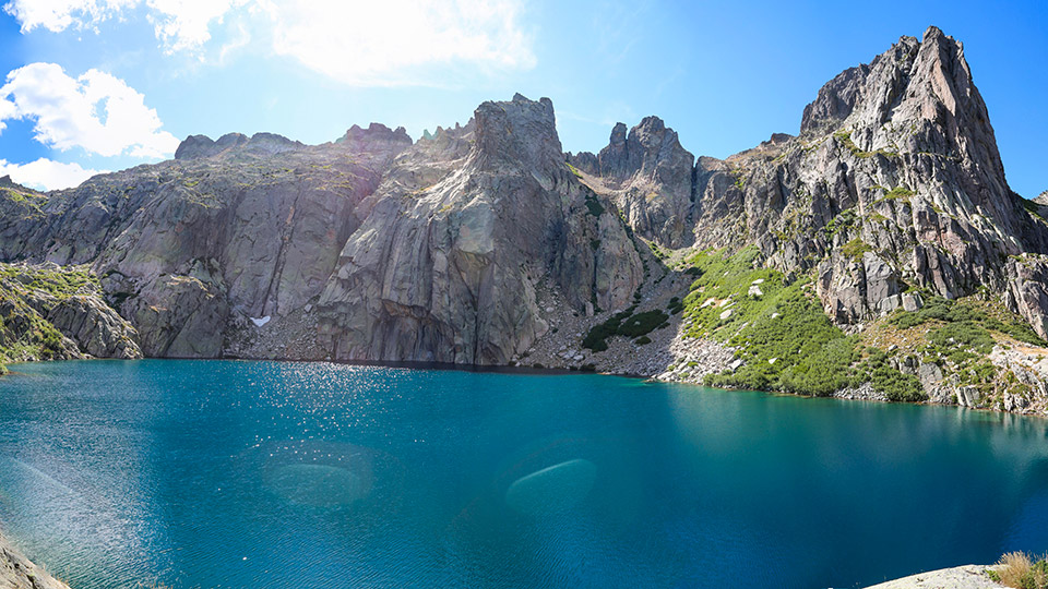 Lac Capitello turquoise entouré de montagnes rocheuses majestueuses avec végétation verdoyante.