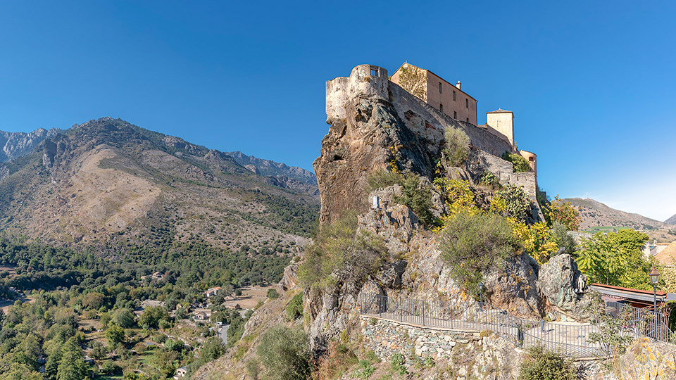 Château historique perché sur une montagne, offrant une vue panoramique des vallées corses.