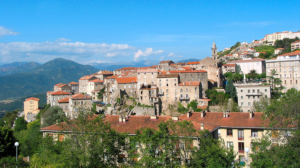 Cette image de Sartène capture l'essence méditerranéenne de la Corse avec ses rues pavées et son architecture en pierre, sous une lumière ensoleillée qui met en valeur un paysage idyllique.