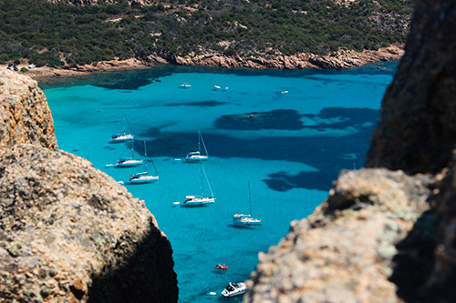 Image de la baie de Roccapina avec ses eaux cristallines et des voiliers, évoquant évasion et tranquillité.