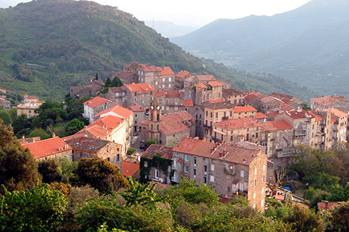 Village pittoresque de Sainte-Lucie de Tallano en Corse, perché sur une colline avec vue sur la vallée, maisons de pierre et toits rouges, entouré de nature verdoyante.