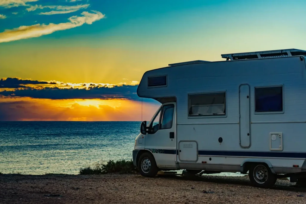 Camping-car face à la mer au coucher du soleil Profil d'un camping-car blanc stationné en bord de mer face à un coucher de soleil lors d'un road trip camping car Corse du Sud.
