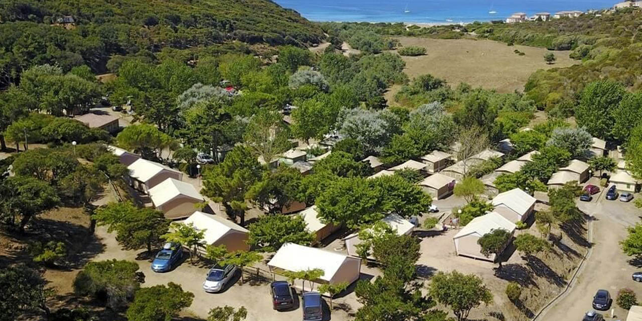 Vue aérienne d'un camping pittoresque en bord de mer avec des cabanes verdoyantes, idéal pour des séjours de détente et d'évasion dans un cadre naturel idyllique.