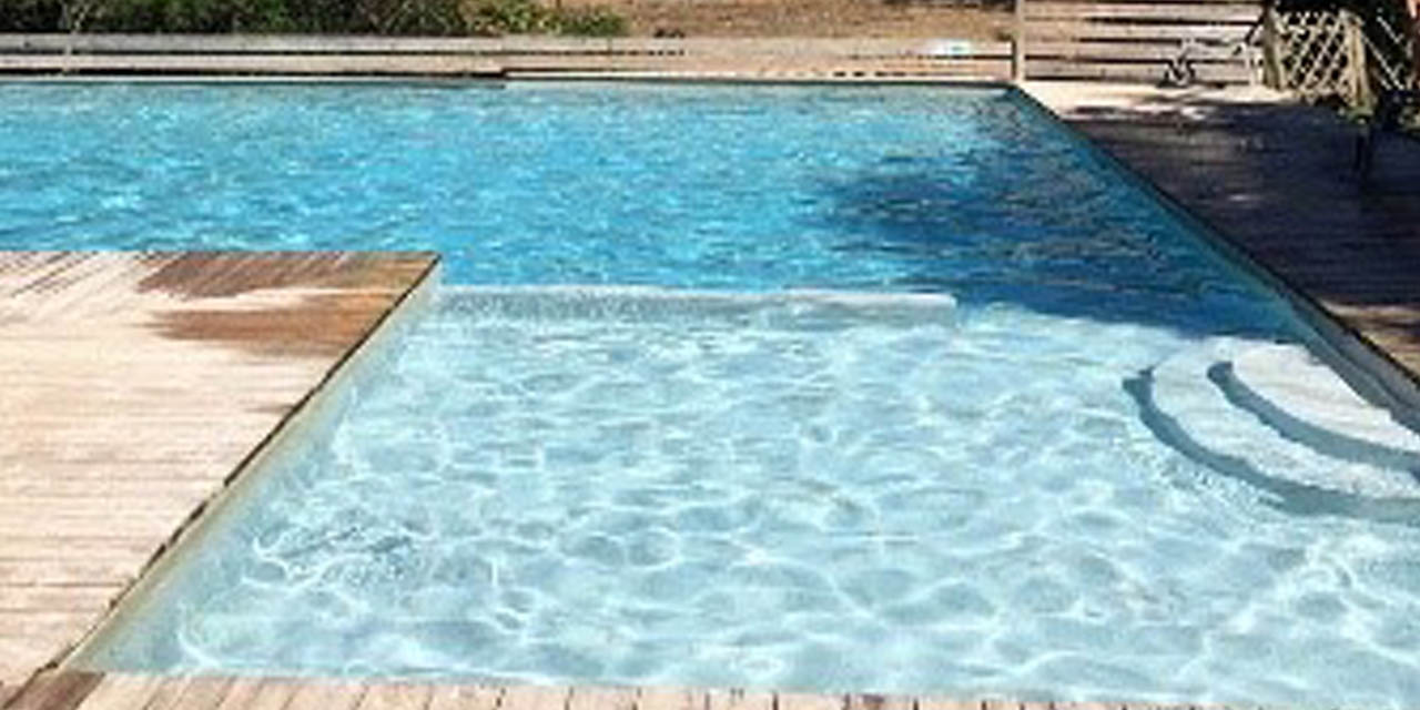 Image d'une piscine bleue étincelante sous le soleil entourée de nature, suggérant relaxation et plaisir estival.