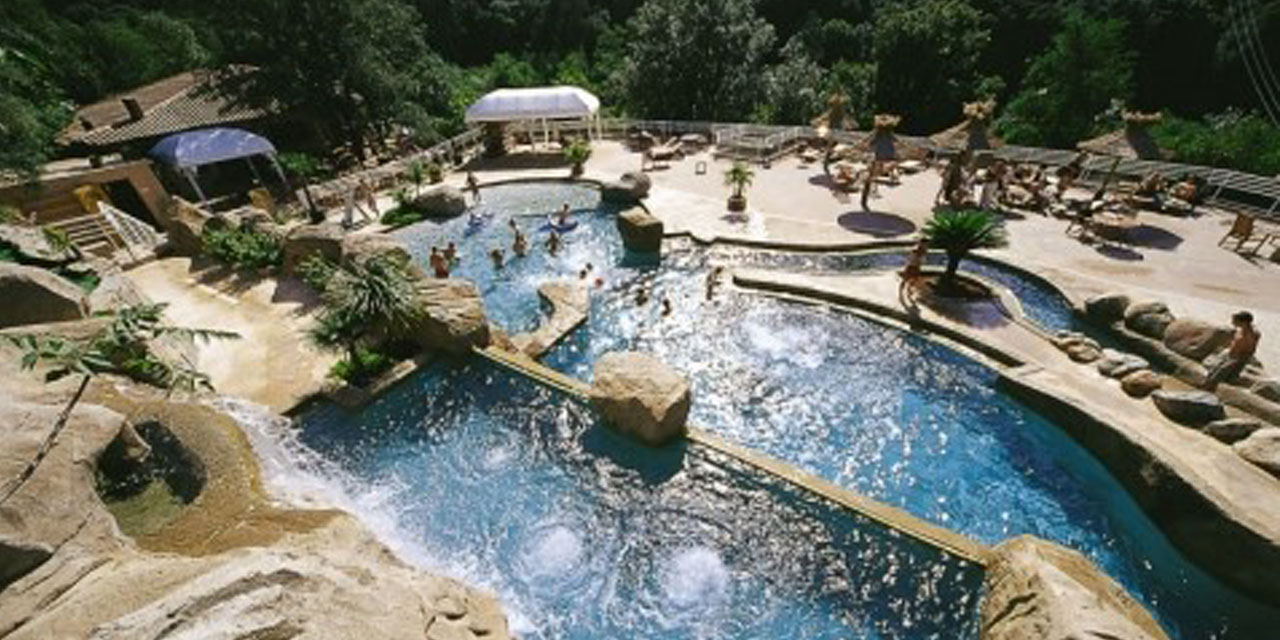 Piscine naturelle entourée de verdure luxuriante avec des aménagements rocheux miroirs au soleil, invitant à l'évasion et à la détente.