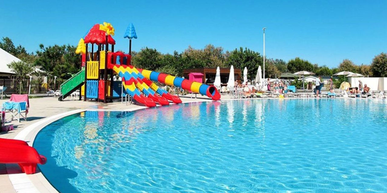 Une piscine entourée de transats et ornée d'une glissade colorée, parfaite pour les jeux aquatiques des enfants et la détente en été sous le soleil radieux.
