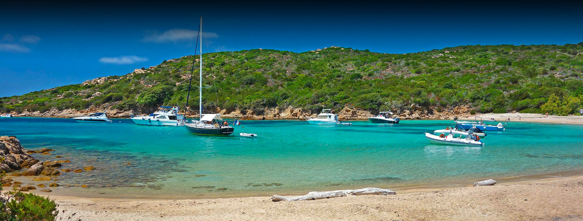 Plage tranquille avec bateaux flottant doucement sur une eau cristalline entourée de verdure, évoquant détente et sérénité.