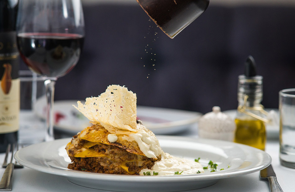 Cette image montre une table élégamment dressée avec un plat sophistiqué accompagné d'un verre de vin rouge, symbolisant l'art culinaire et la convivialité.