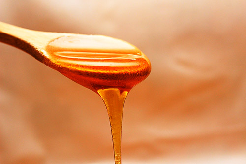 Photographie d'une cuillère en bois recouverte de miel doré, capturant sa brillance et sa texture invitante pour éveiller la gourmandise naturelle.