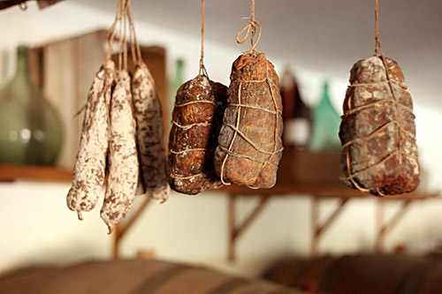 Cette image présente une sélection de charcuteries artisanales suspendues dans une ambiance rustique, illustrant le savoir-faire traditionnel et l'art local.