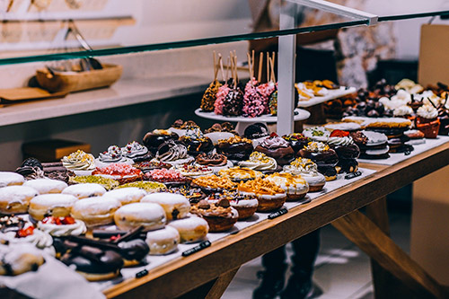 Vitrine de desserts sucrés variés et colorés avec des donuts décorés, évoquant une ambiance festive et gourmande.