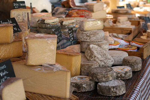 Cette image illustre une scène vivante sur un marché, remplie de fromages artisanaux de qualité qui séduisent les amateurs, capturant l'essence et la diversité de la gastronomie locale.