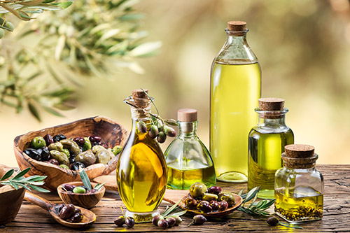 Une variété d'huiles d'olive artisanales est exposée sur une table en bois, éclairée par la lumière naturelle, évoquant la fraîcheur et le savoir-faire traditionnel en pleine nature.