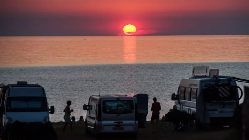 coucher-soleil-camping-corsica-camping Coucher de soleil sur la mer avec camping-cars et silhouettes sur un spot en bord de plage en Corse