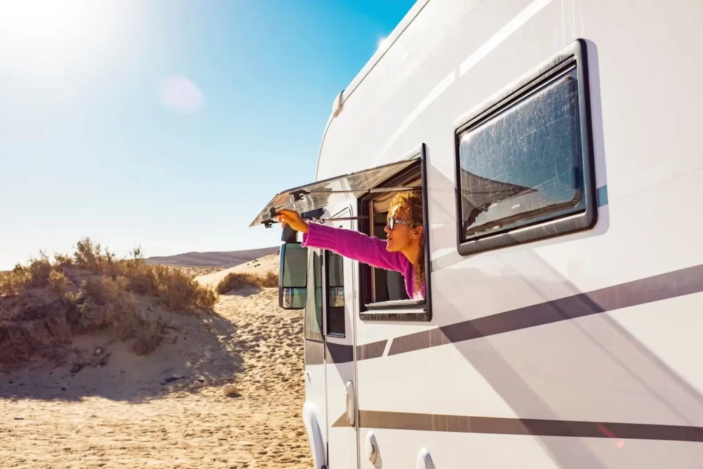 Road trip en camping-car – esprit vanlife Femme à la fenêtre d’un camping-car pointant l’horizon, dunes de sable et ciel bleu