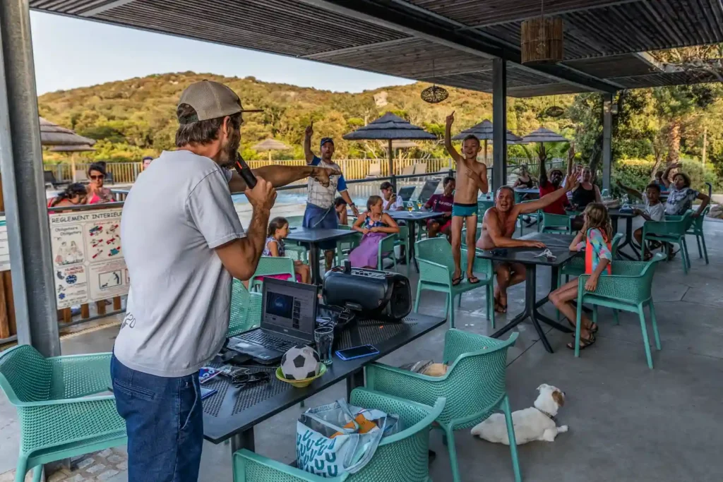 camping-le-damier-animation-activité-loisir Animateur micro en main organisant un jeu avec des vacanciers sur la terrasse du Camping Le Damier.