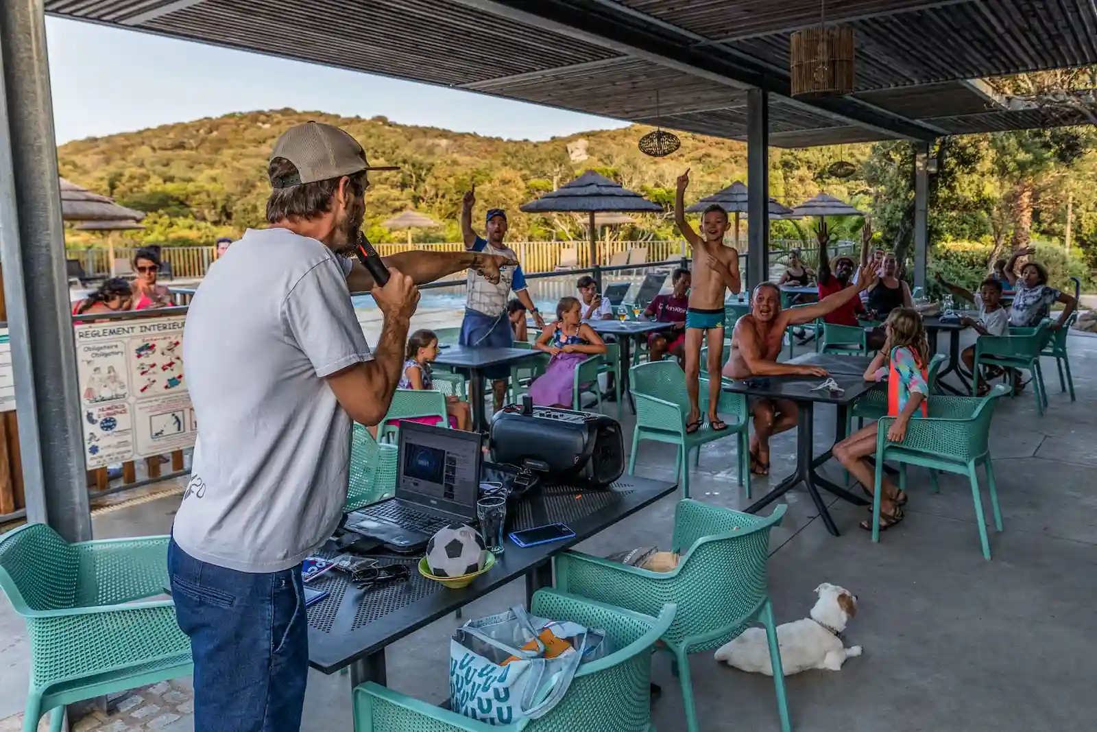 Animateur micro en main organisant un jeu avec des vacanciers sur la terrasse du Camping Le Damier.