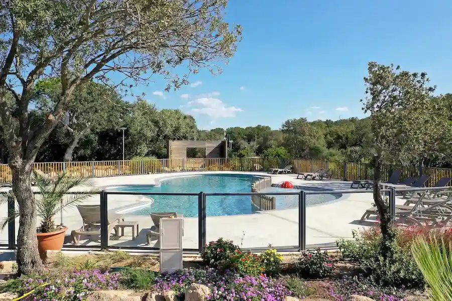Vue paysagère de la piscine sécurisée du Camping Le Damier, entourée de végétation méditerranéenne et de chênes.