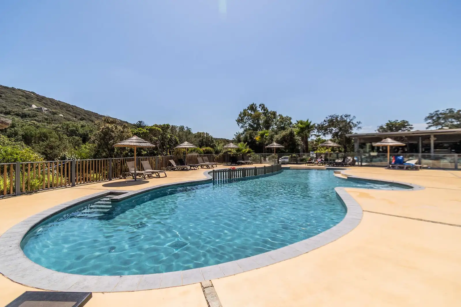 Grande piscine extérieure avec transats et parasols en paille au Camping Le Damier, Corse du Sud.