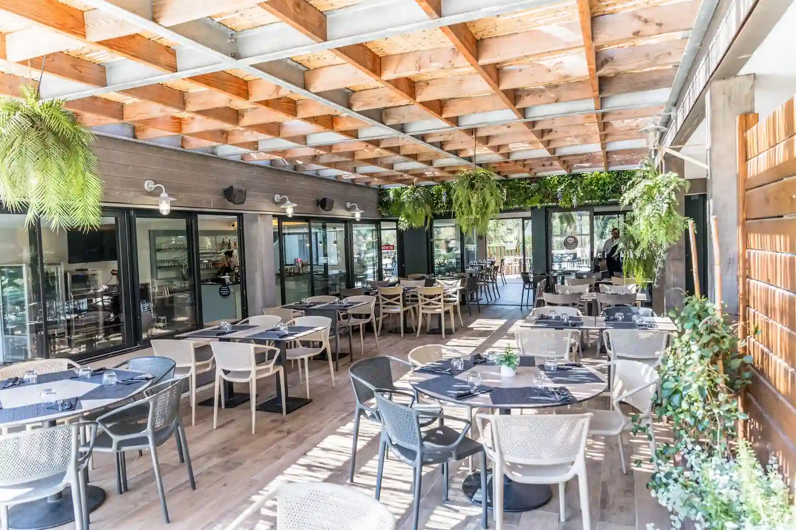 Terrasse ombragée du restaurant du Camping Le Damier avec mobilier moderne et décoration végétale.