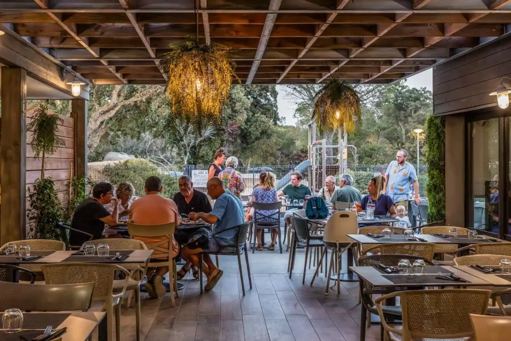 camping-le-damier-salle-restaurant Clients dînant le soir sur la terrasse éclairée du restaurant du Camping Le Damier en Corse du Sud.