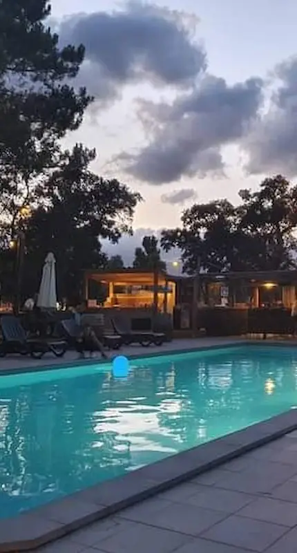Piscine illuminée du Camping U Stabiacciu à la tombée de la nuit avec transats et bar lounge en arrière-plan.