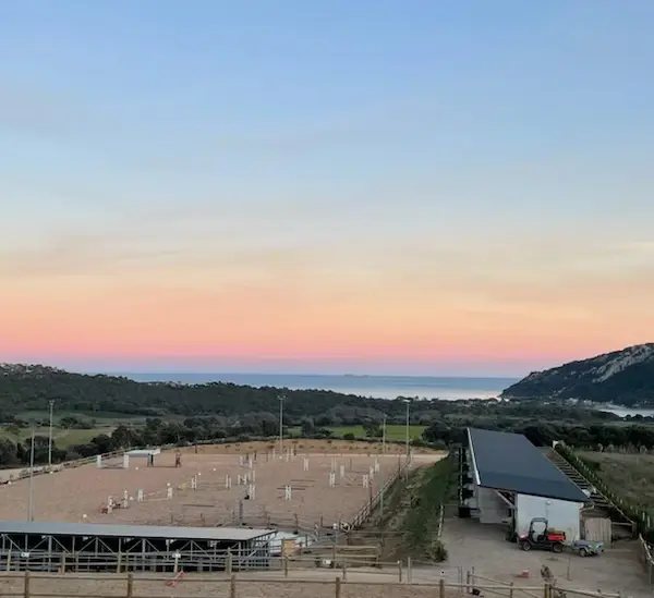 Vue panoramique du domaine équestre Equicomplice au coucher du soleil avec carrière de saut d'obstacles, écuries modernes et vue imprenable sur la mer Méditerranée en Corse du Sud.