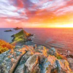 Silhouette des Îles Sanguinaires et de la tour génoise d'Ajaccio sous un ciel flamboyant au crépuscule.