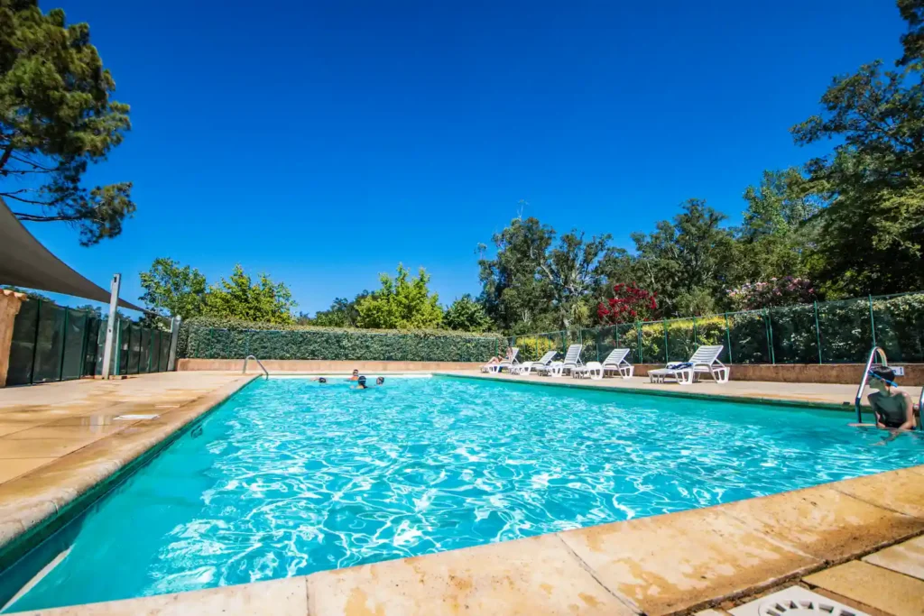 piscine-ensoleillee-camping-santa-lucia-corse Large piscine rectangulaire à débordement visuel avec eau turquoise, entourée de transats et d'une forêt de chênes verts au Camping Santa Lucia en Corse-du-Sud.
