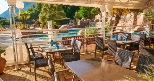 prestations-camping-les-oliviers Tables dressées sous une pergola sur la terrasse du restaurant avec vue sur la piscine et les rochers.