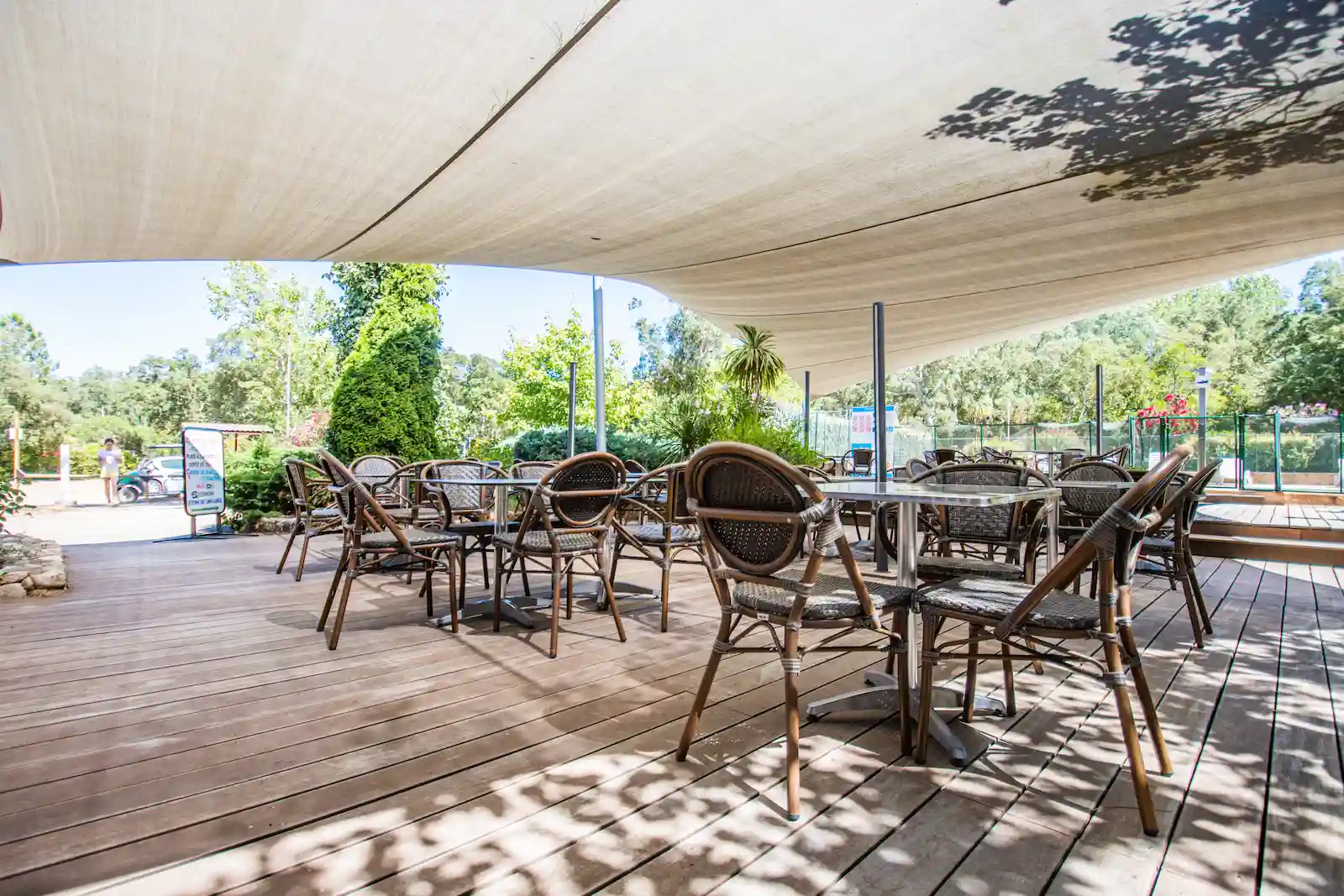 Terrasse du restaurant du camping avec voile d'ombrage blanche et vue sur l'espace piscine.