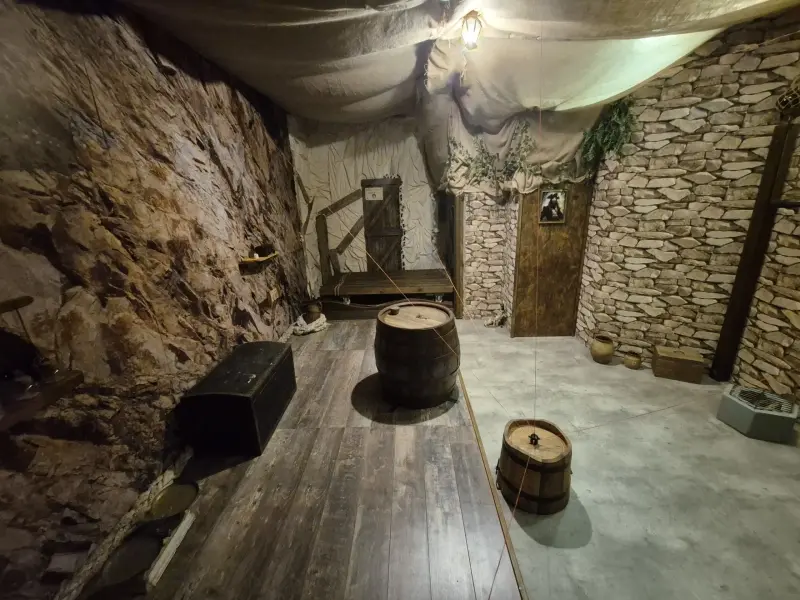 Salle d'immersion pirate avec murs en roche, coffre au trésor et tonneaux en bois dans un escape game à Porto.