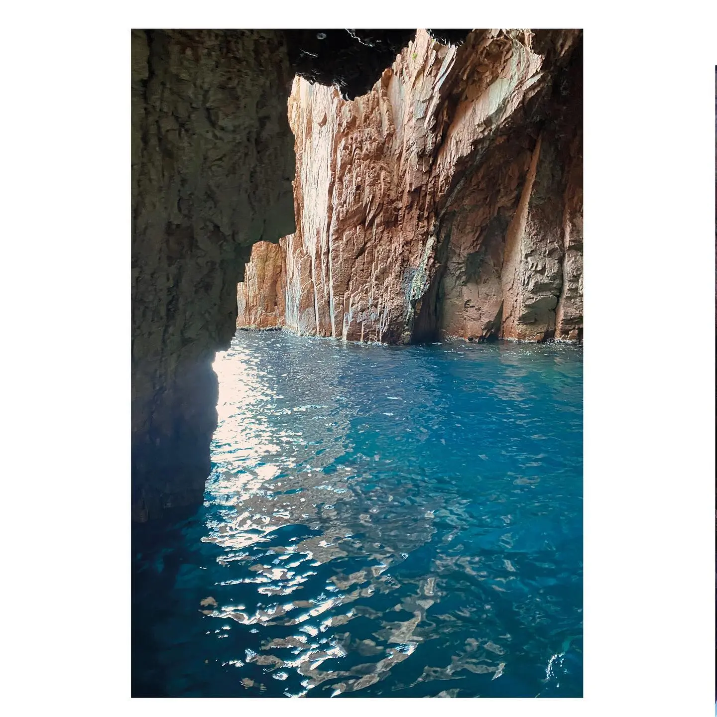 Intérieur d'une grotte marine spectaculaire aux parois rocheuses rouges et ocres, baignée par une eau bleu turquoise scintillante lors d'une balade en bateau en Corse du Sud près de Piana.