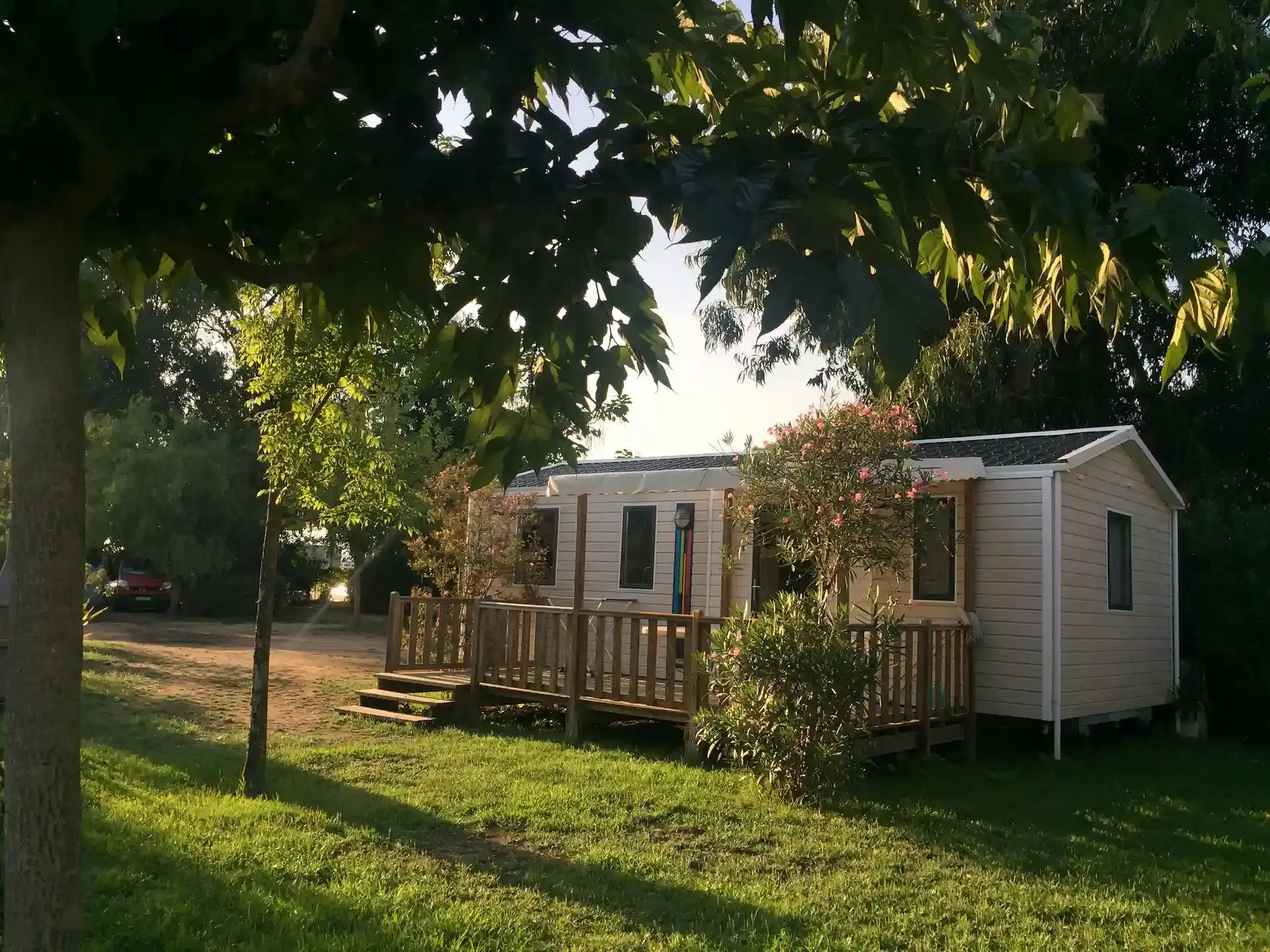 Un mobile-home moderne avec terrasse en bois au Camping Milella à Propriano, Corse-du-Sud, baigné par la lumière dorée du coucher de soleil sous les arbres.