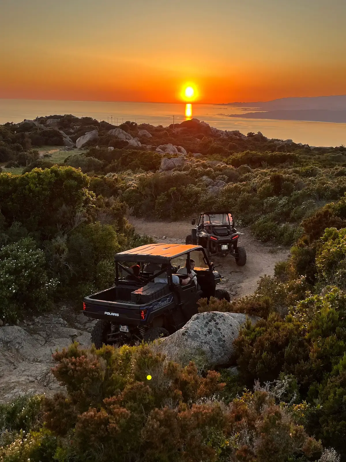 Deux buggies tout-terrain surplombant une baie méditerranéenne sous un soleil couchant doré depuis les hauteurs du maquis.