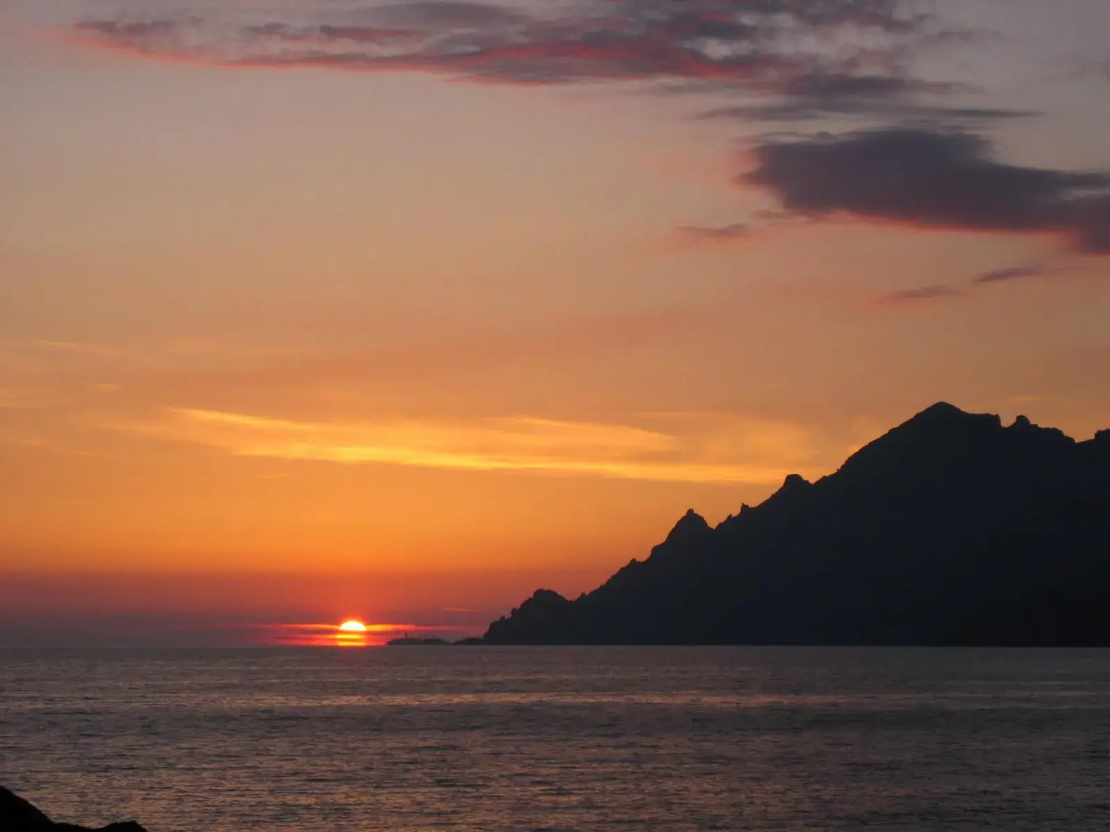 Coucher de soleil flamboyant sur la mer Méditerranée avec la silhouette d'une montagne côtière en Corse.