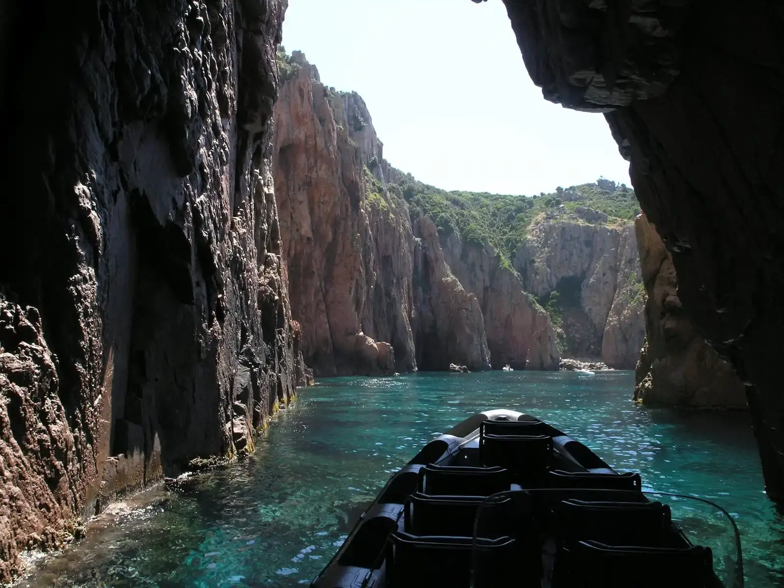 Vue depuis un bateau entrant dans une crique étroite aux parois rocheuses avec une eau cristalline turquoise.