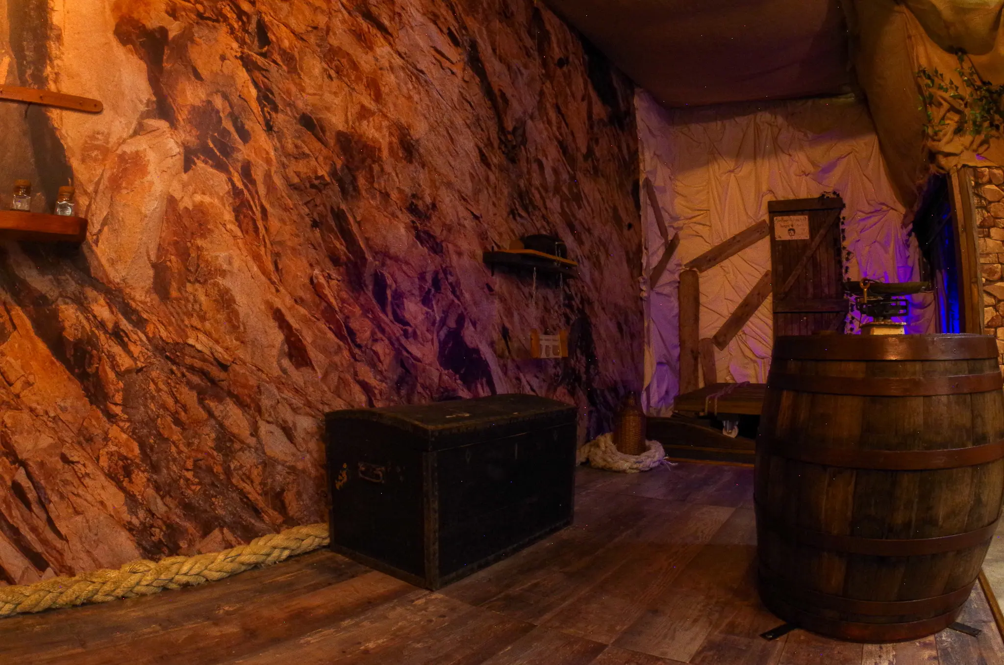 Décor d'une cale de navire avec coffre noir, cordages et murs rocheux pour un escape game familial.