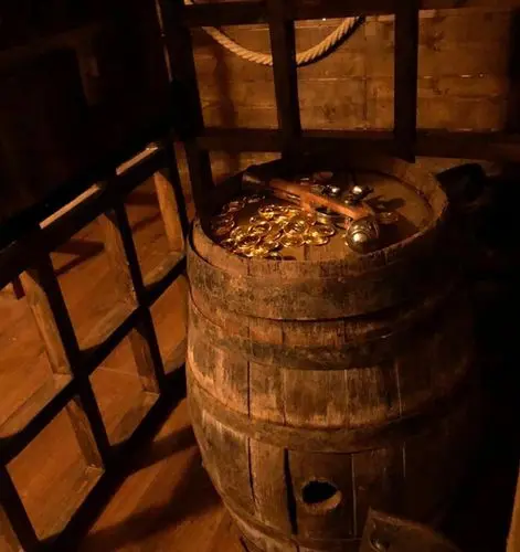 Détail d'un tonneau en bois surmonté de pièces d'or et d'un pistolet de pirate ancien sous une lumière tamisée.