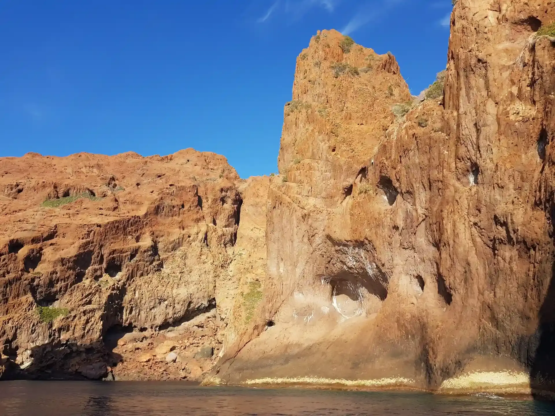Hautes falaises de granit rouge sculptées par l'érosion sous un ciel bleu sans nuage en Corse.