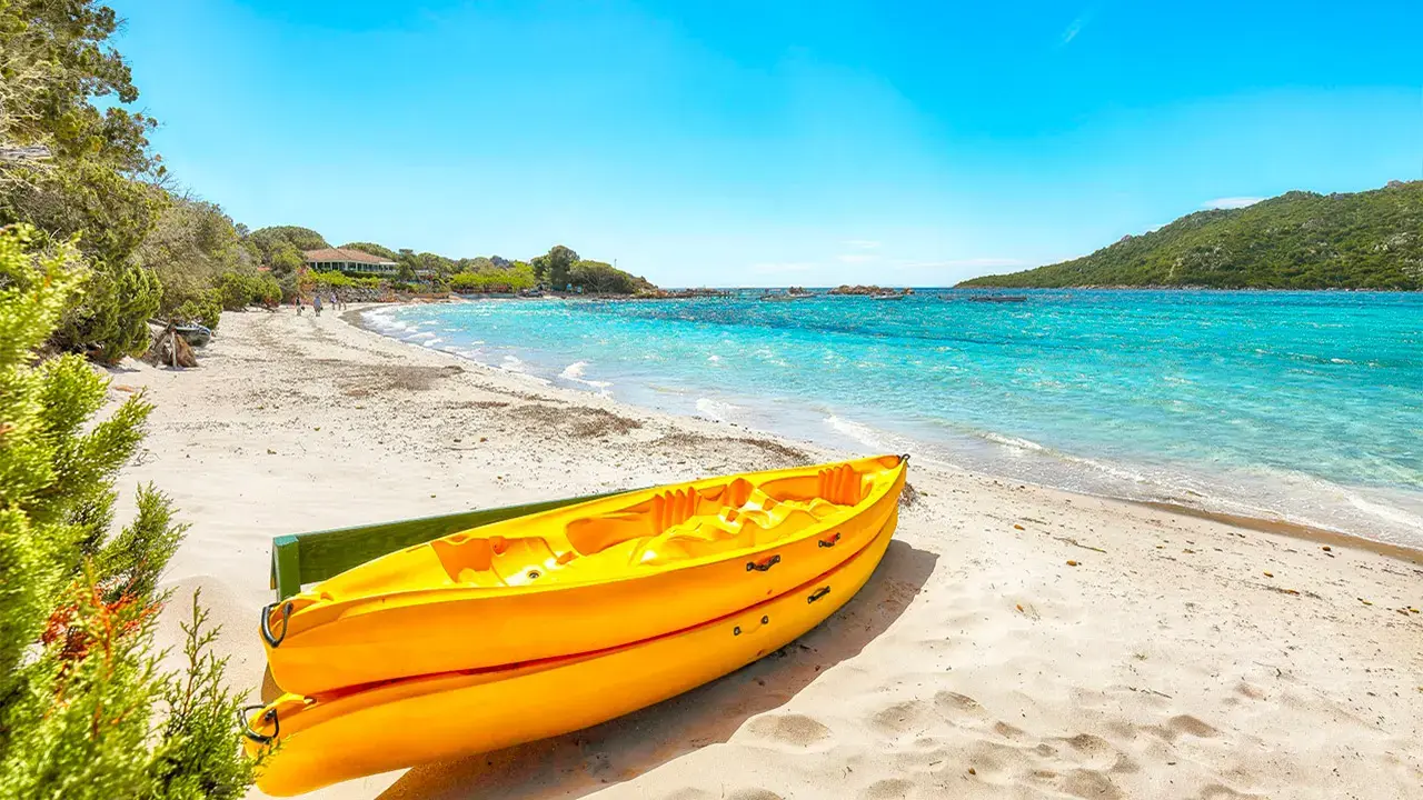 Deux kayaks de mer jaunes posés sur le sable blanc de la plage de Pinarello en Corse-du-Sud, avec une eau turquoise et des collines verdoyantes en arrière-plan.