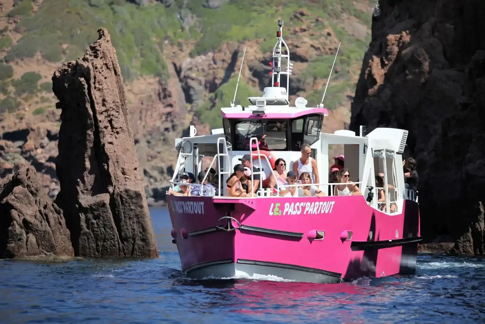 Le bateau Le Pass'Partout III pénétrant à l'intérieur d'une grotte marine aux parois de granit rouge dans les Calanques de Piana.