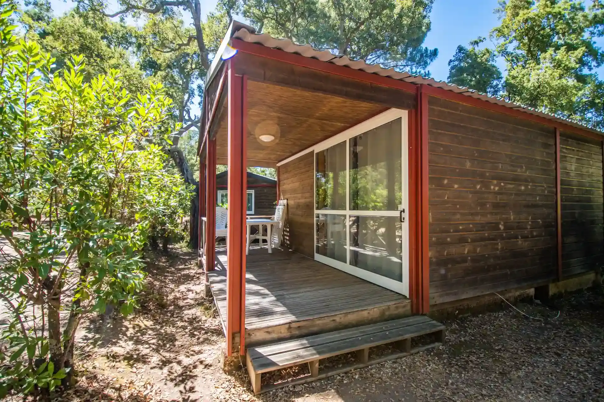 Bungalow en bois moderne avec terrasse couverte et baie vitrée niché dans la forêt.