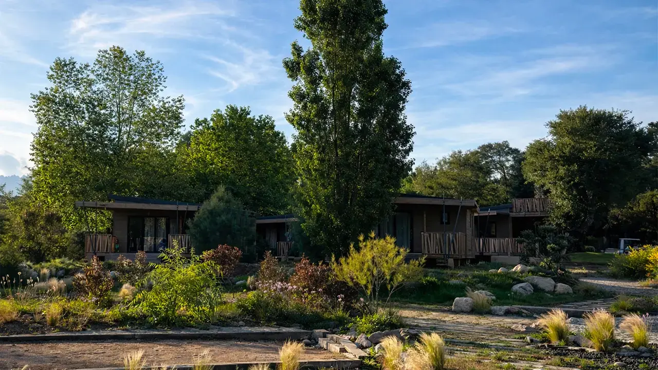 Lodges de luxe en bois avec terrasses privées au Camping U Pinarellu, nichés au cœur d'un jardin méditerranéen paysager sous un ciel bleu.